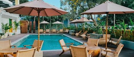 A poolside area with lounge chairs and umbrellas, surrounded by greenery.
