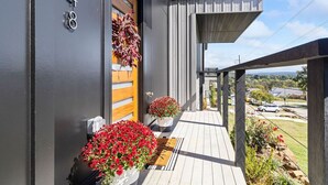 A modern house with a wooden door, a balcony with potted plants, and a view of the neighborhood.