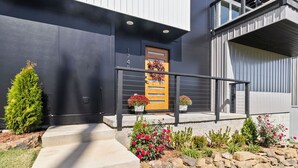 A modern house with a dark facade, a wooden door, and a stone pathway leading to the entrance.