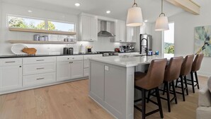 A modern kitchen with white cabinetry, a large island with bar stools, and pendant lighting.