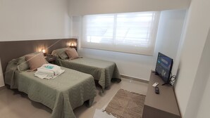 Een kamer met twee bedden, een televisie en een raam met jaloezieën.