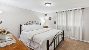 Ein Schlafzimmer mit Bett, Nachttisch, Lampe und Vorhängen.