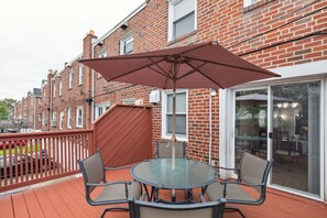Eine Terrasse mit Glastisch und Stühlen, ein Holzboden und ein Ziegelgebäude im Hintergrund.
