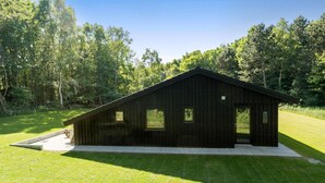 Un rustico chalet di legno con tetto spiovente, ampie finestre e fondamenta in cemento.