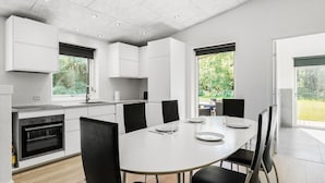 Una cucina moderna con mobili bianchi, forno a incasso e zona pranzo con tavolo bianco e sedie nere.