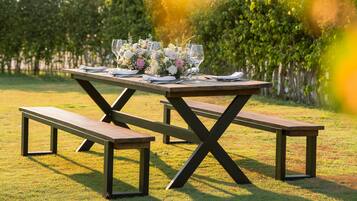 A picnic table set outdoors with a floral centerpiece and wine glasses.