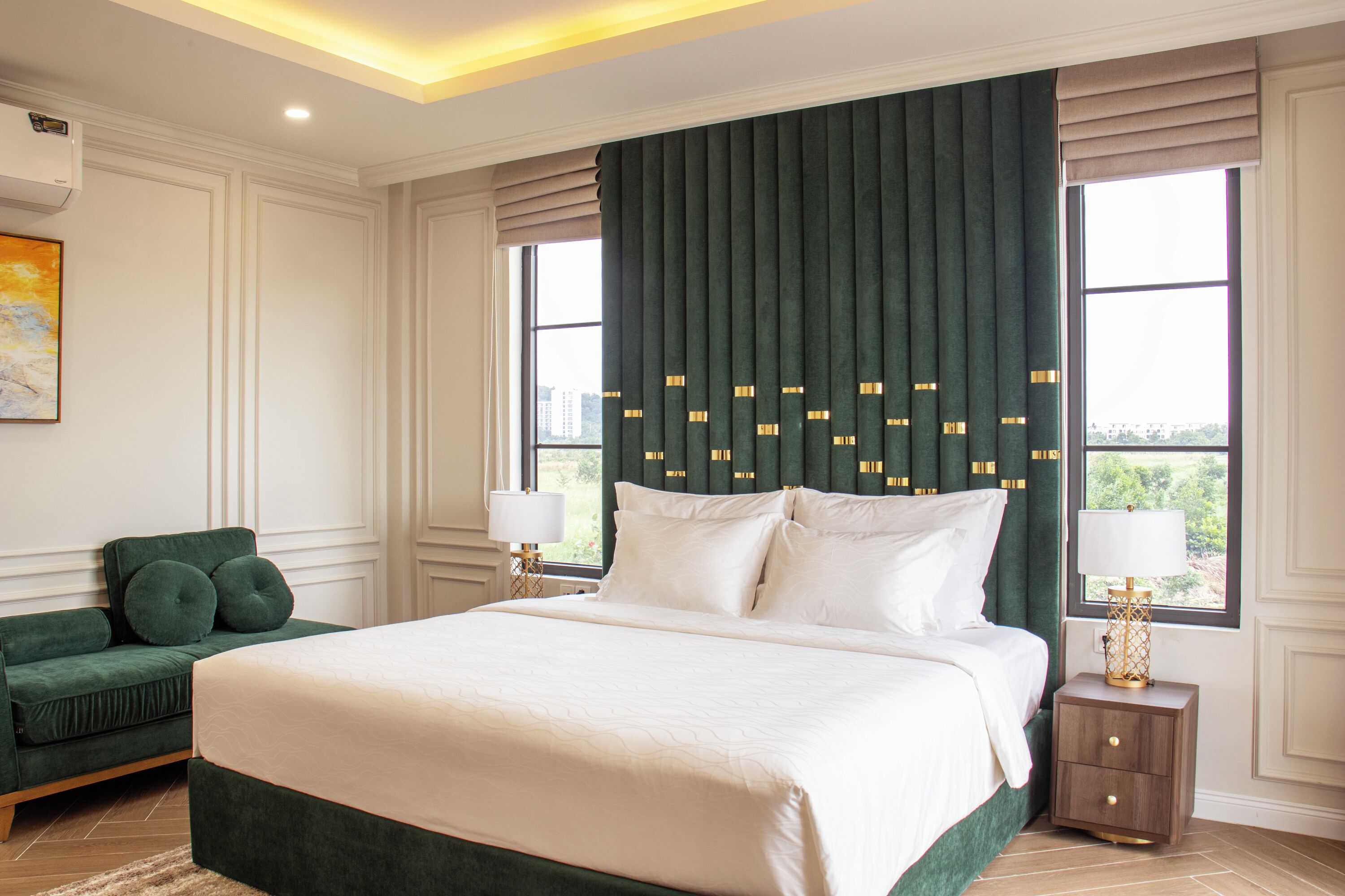 A bedroom with a large bed, two bedside tables with lamps, a green sofa, and a window with curtains.