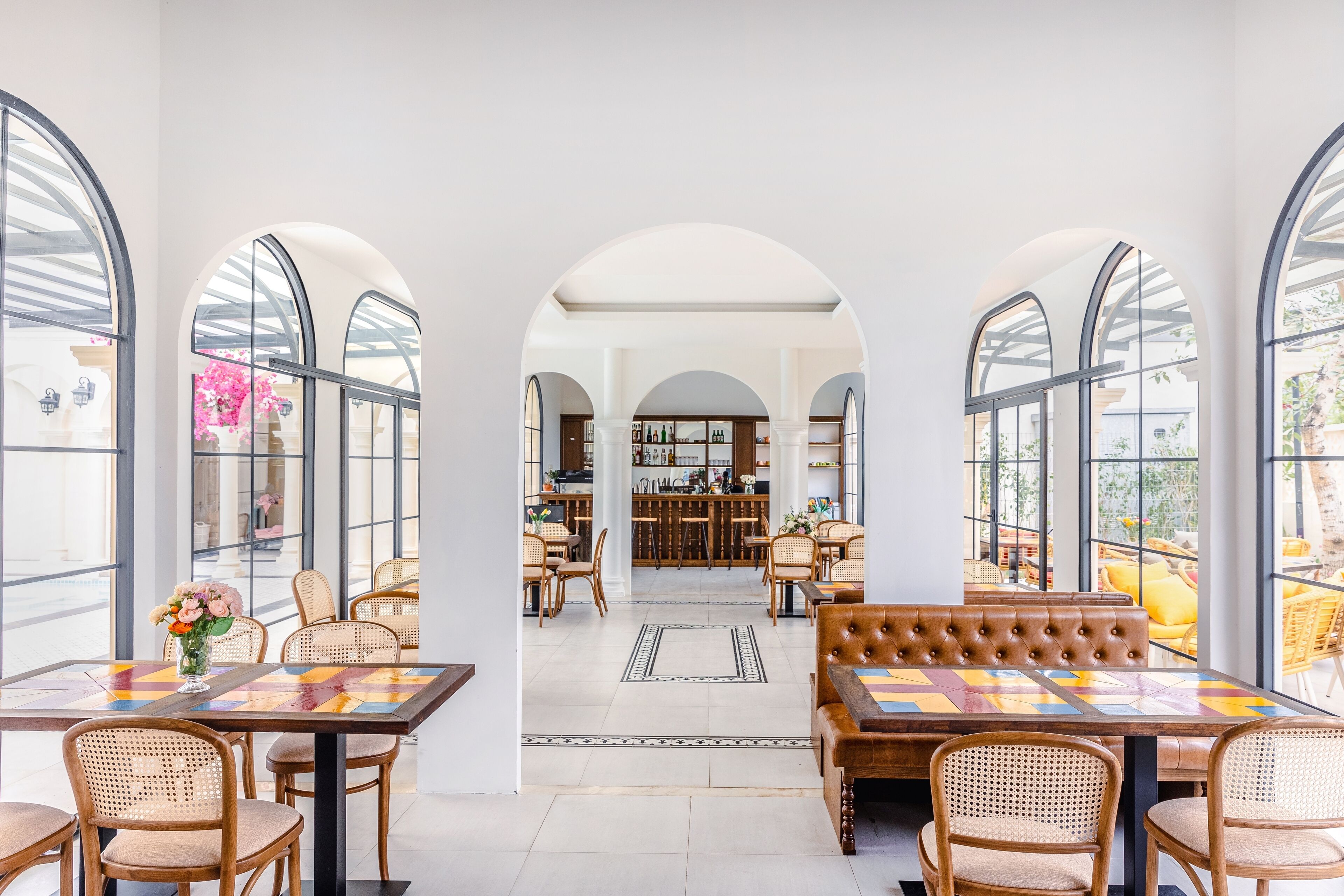 A spacious dining area with high arched windows, wicker furniture, and a central bar area.