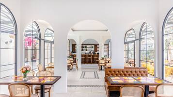 A spacious dining area with high arched windows, wicker furniture, and a central bar area.