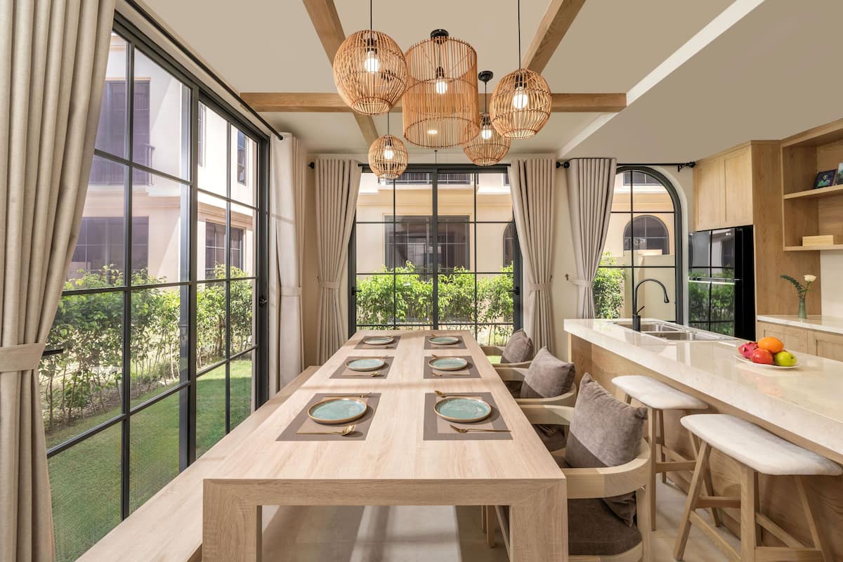 Una cocina moderna con una isla grande, un comedor con una mesa larga y ventanas amplias con vistas al exterior.