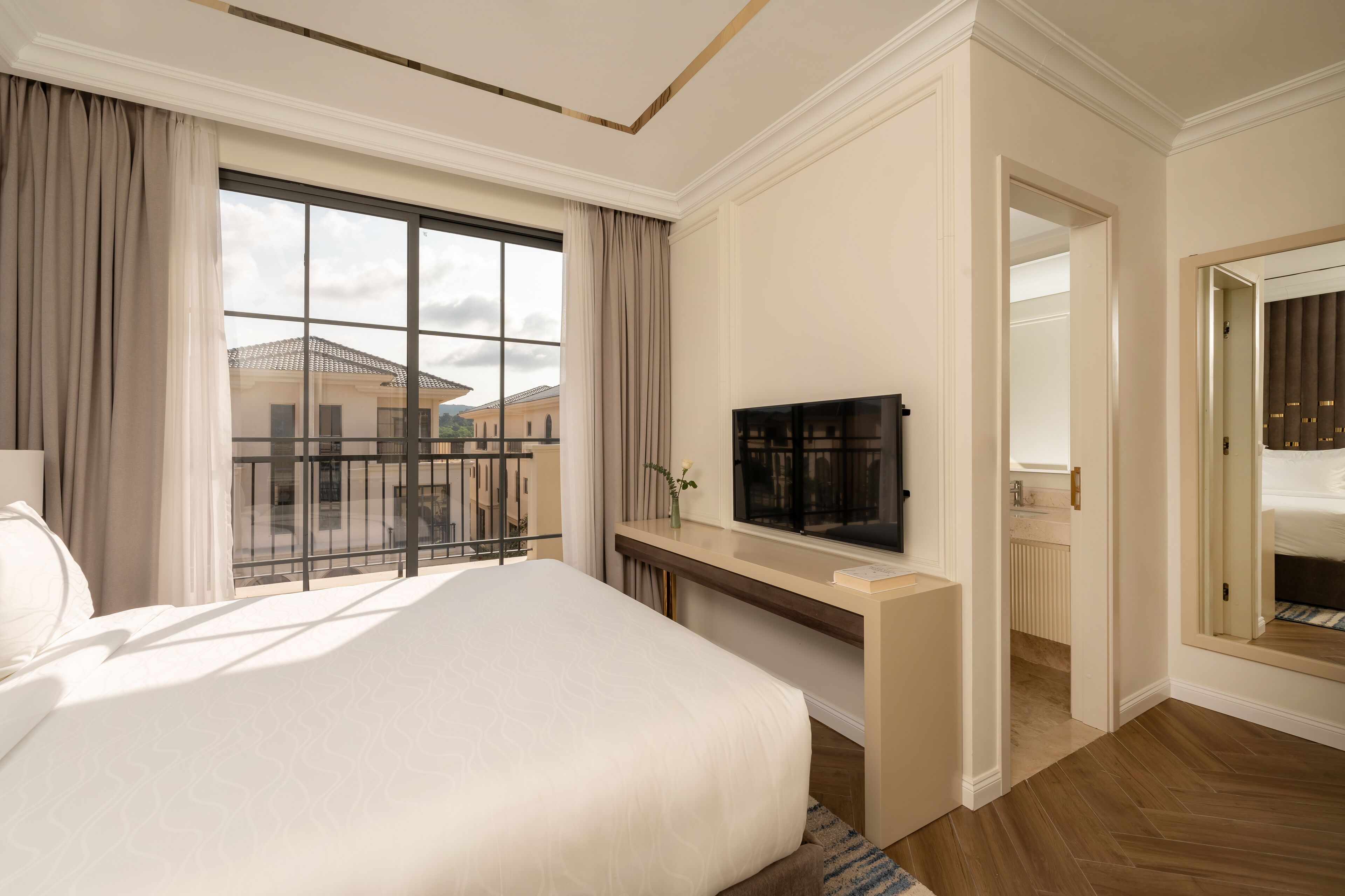 Quarto de hotel com uma cama grande, televisão, escrivaninha e vista para o exterior.