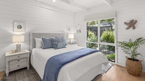 Ein Schlafzimmer mit Bett, Nachttischen, Deckenventilator, Fenster mit Blick auf Grünflächen und einer Meerstern-Dekoration.