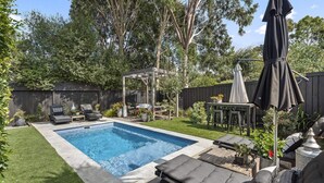 Ein Garten mit Schwimmbad, einer Pergola, Sitzgelegenheiten im Freien und einem Grillplatz.
