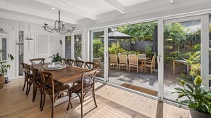 Ein großzügiger Essbereich mit Holztisch und Stühlen, große Schiebeglasfenster, die zu einer Terrasse mit Gartenblick führen.
