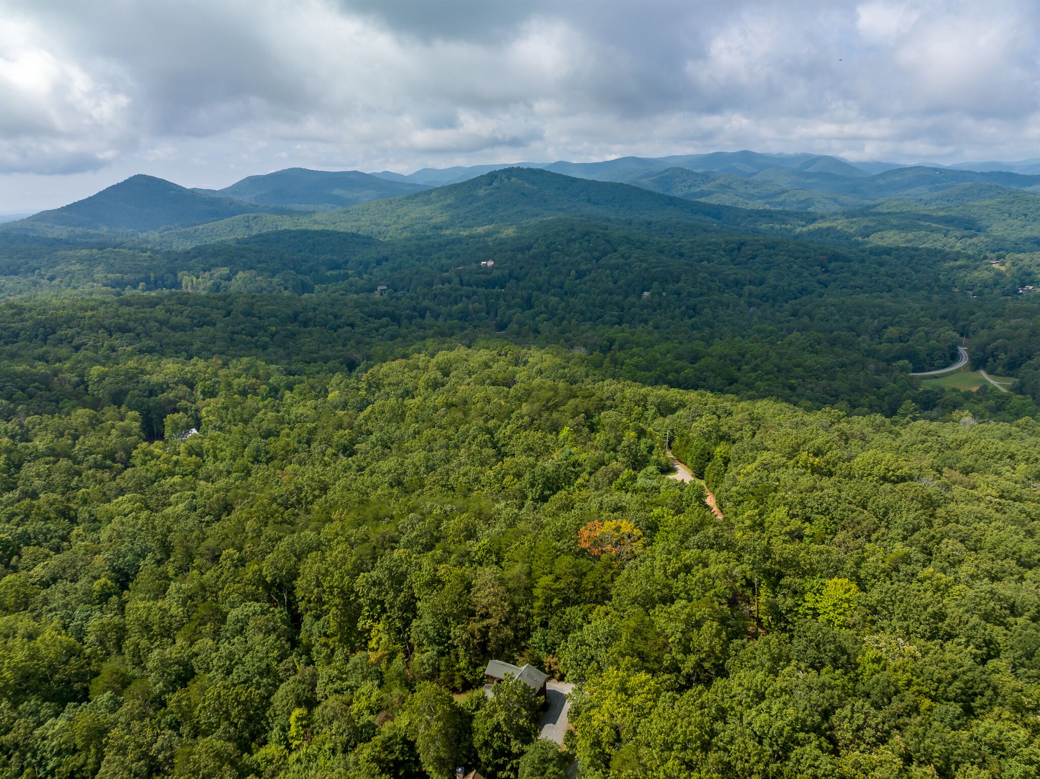 A dense forested landscape with a winding road and a small building in the foreground.