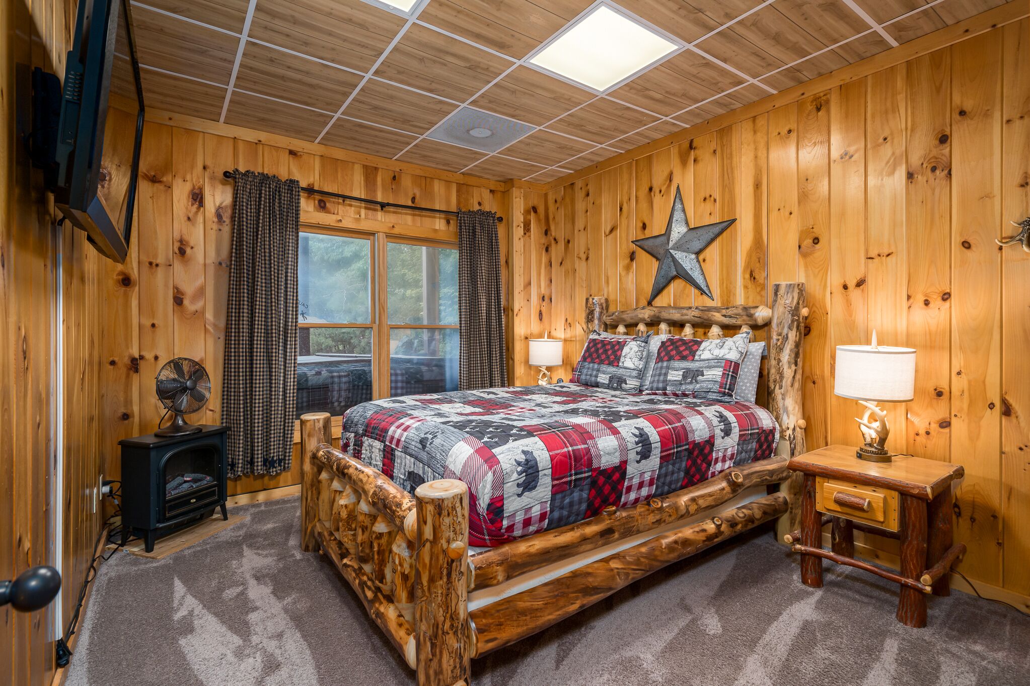 Quarto de cabana de madeira com cama, um enfeite de estrela, um ventilador e uma luminária.