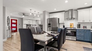 A modern kitchen with white cabinets, a stainless steel refrigerator, and a dining area with a table set for four.