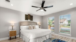 A bedroom with a bed, bedside lamps, a ceiling fan, and large windows.