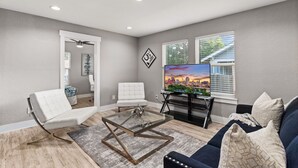 A living room with a glass coffee table, white and blue chairs, a dark blue sofa, and a TV on a black stand.