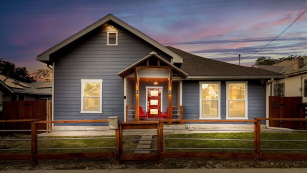 A two-story house with a front porch, a red door, and a small front yard.