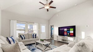 Ein modernes Wohnzimmer mit einem großen Flachbildfernseher, einem Deckenventilator und Bergblick durch die Fenster.