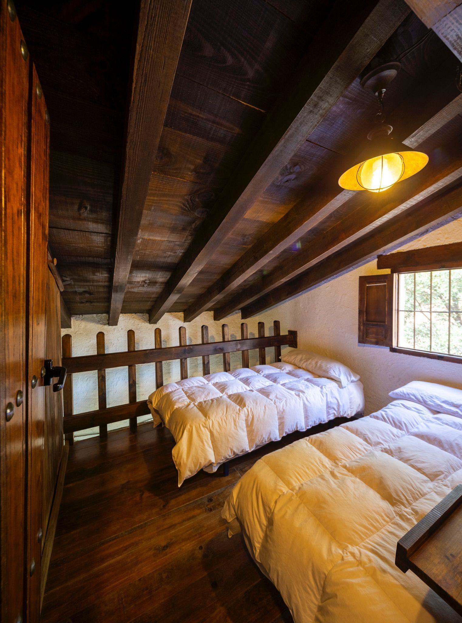A rustic wooden room with two beds, a wooden ceiling, and a window.