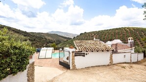 Um edifício branco com telhado de telhas e uma parede de pedra, piscina e vista para colinas verdes.