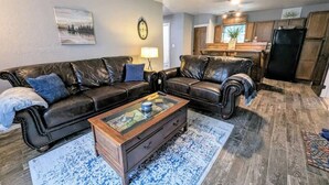A living room with a black leather sofa set, a wooden coffee table, and a patterned rug. - Rustic Bungalow - Rugged with a Touch of Class (Sulphur)