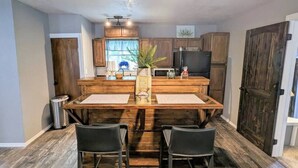 A kitchen with a central island, wooden cabinets, and a dining area with two chairs. - Rustic Bungalow - Rugged with a Touch of Class (Sulphur)
