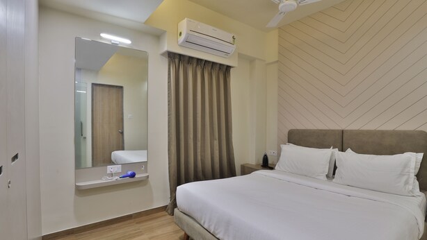 A modern bedroom with a large bed, an air conditioning unit, a ceiling fan, a mirror, and a bedside table. - hotel monville  (Vadodara)