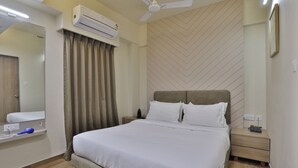 A neatly arranged bedroom with a bed, bedside tables, an air conditioner, a ceiling fan, and a mirror. - hotel monville  (Vadodara)
