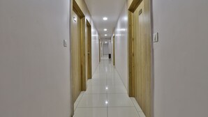 A long, narrow hallway with wooden doors on both sides and a tiled floor. - hotel monville  (Vadodara)