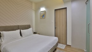 A bedroom with a bed, a nightstand, a door, and a wall-mounted artwork. - hotel monville  (Vadodara)