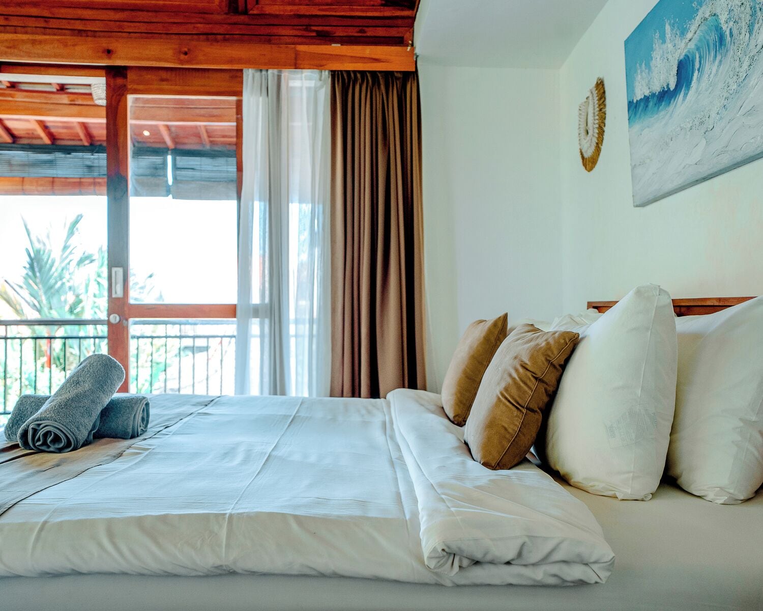 A hotel room with a bed, pillows, a painting, and a view through a window.