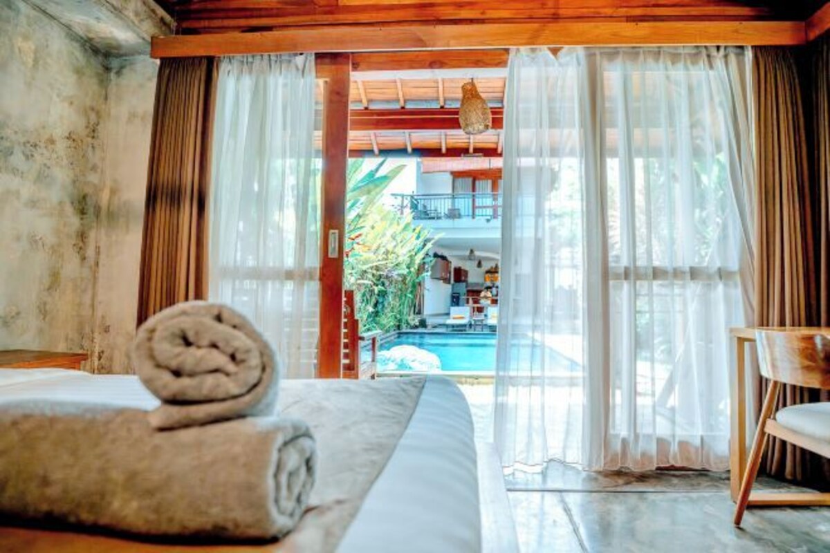 Ein Zimmer mit Bett, Sessel und Blick auf Pool und Außenbereich.