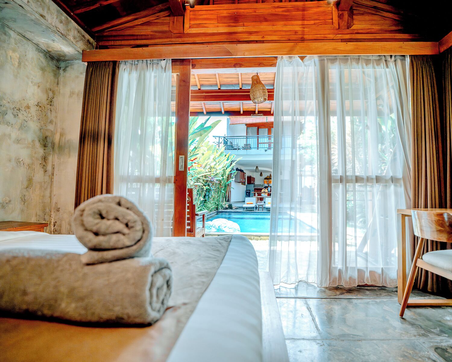 Habitación con cama, techo de madera, vista a una piscina y un balcón.