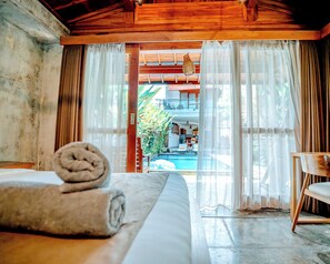 A room with a bed, a wooden ceiling, a view of a pool, and a balcony. - Kubu D'Carik Villa & Bungalow (Munggu)