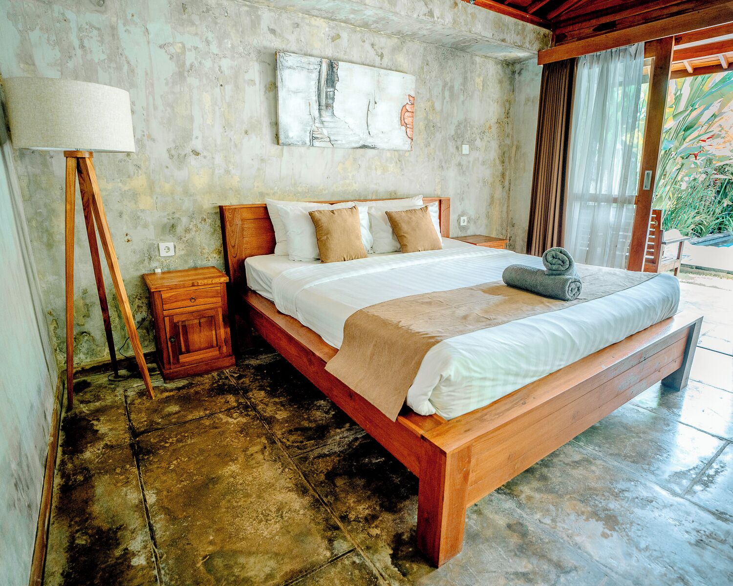A bed with a wooden frame, a bedside table, a lamp, and a painting on the wall.