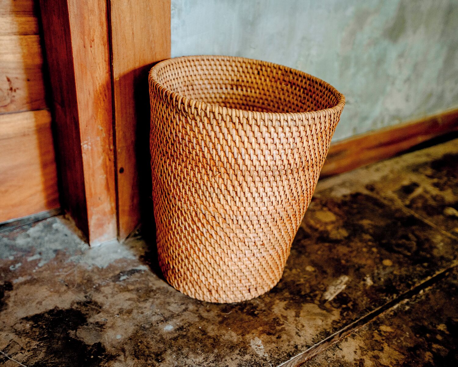 Una cesta tejida apoyada contra una pared, junto a un suelo de madera.