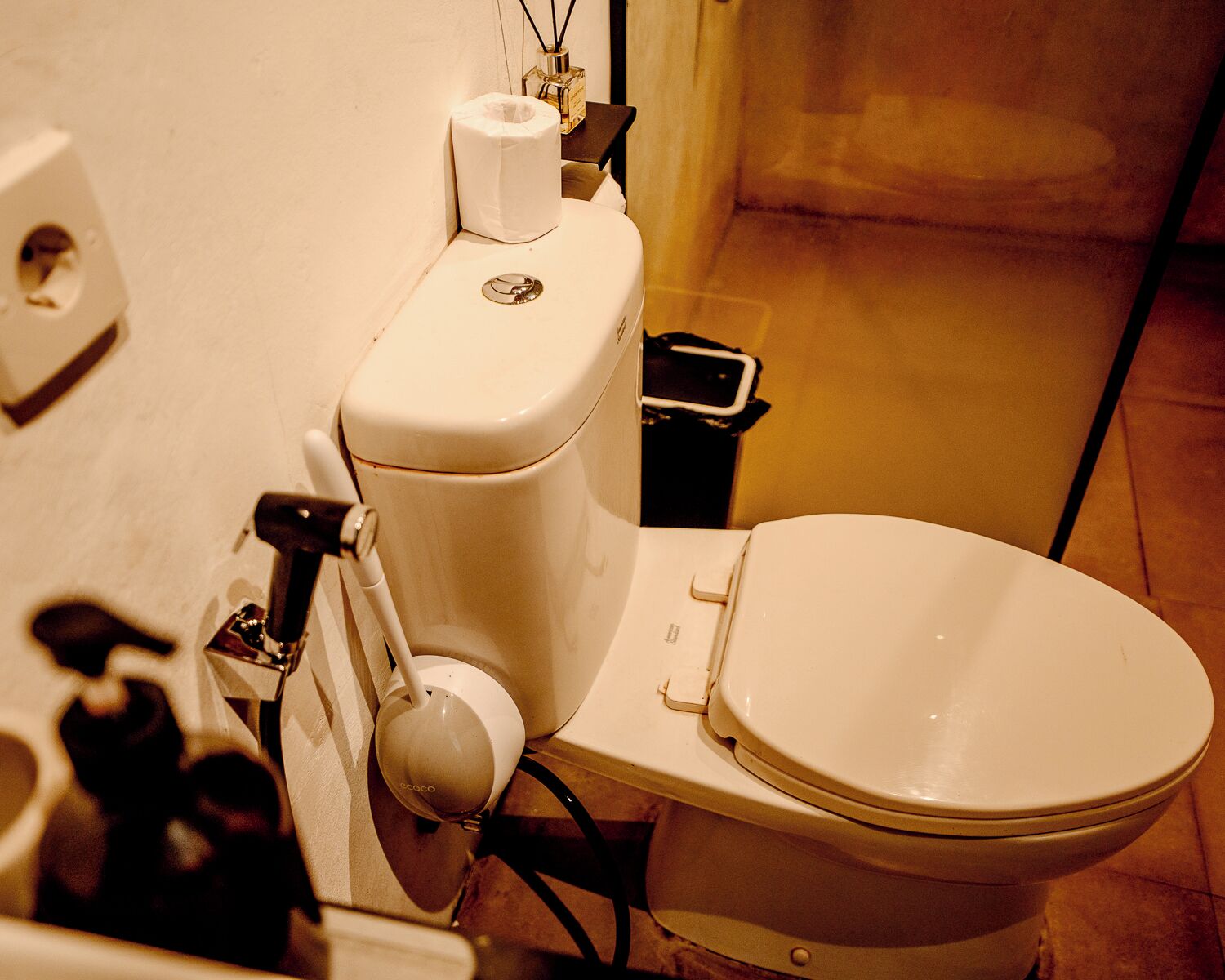 Toilet met een bidetopstuk, een wc-rol en een smartphone op een klein tafeltje ernaast.
