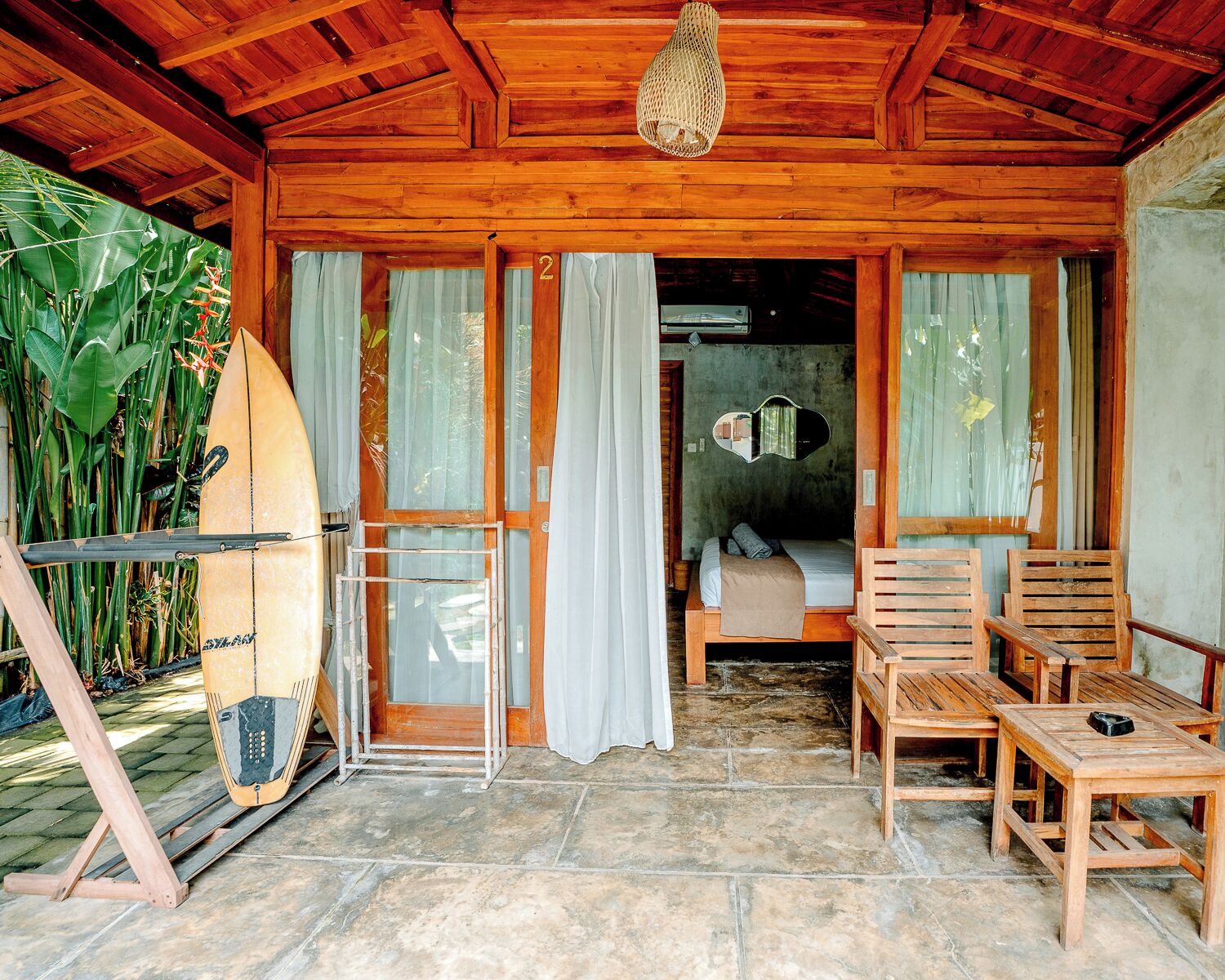 A wooden cabin with a bed, a surfboard, and a chair.