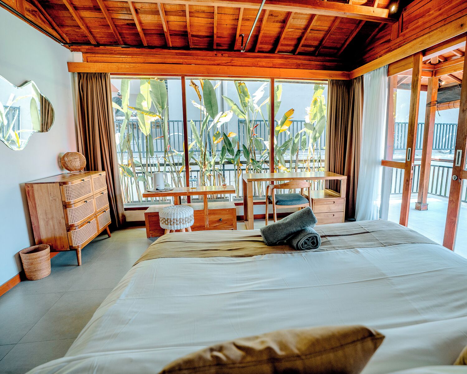 Una habitación con cama, muebles de madera, ventana con vista a palmeras y un balcón.