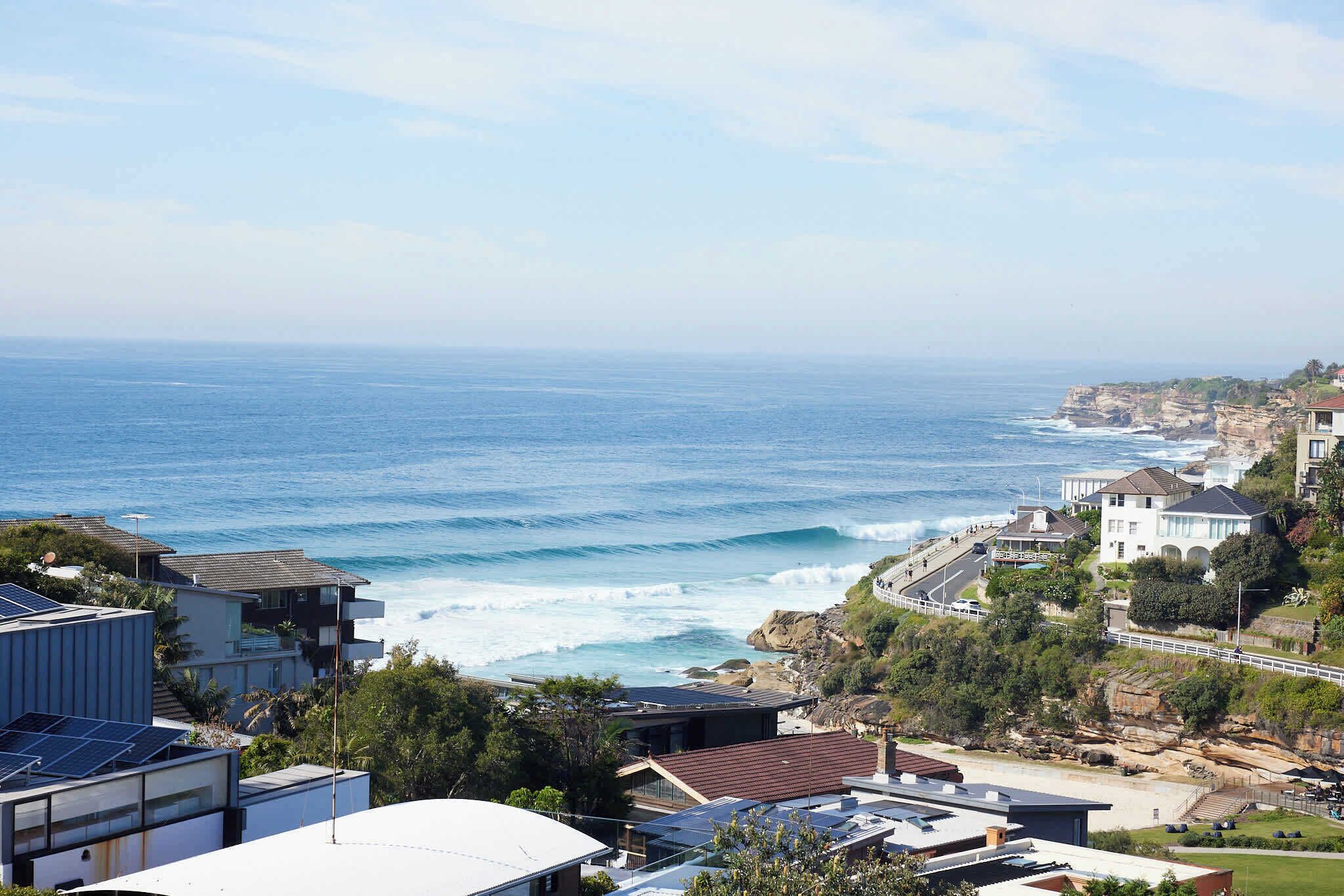 A coastal residential area with modern houses, a view of the ocean, and a paved walkway.