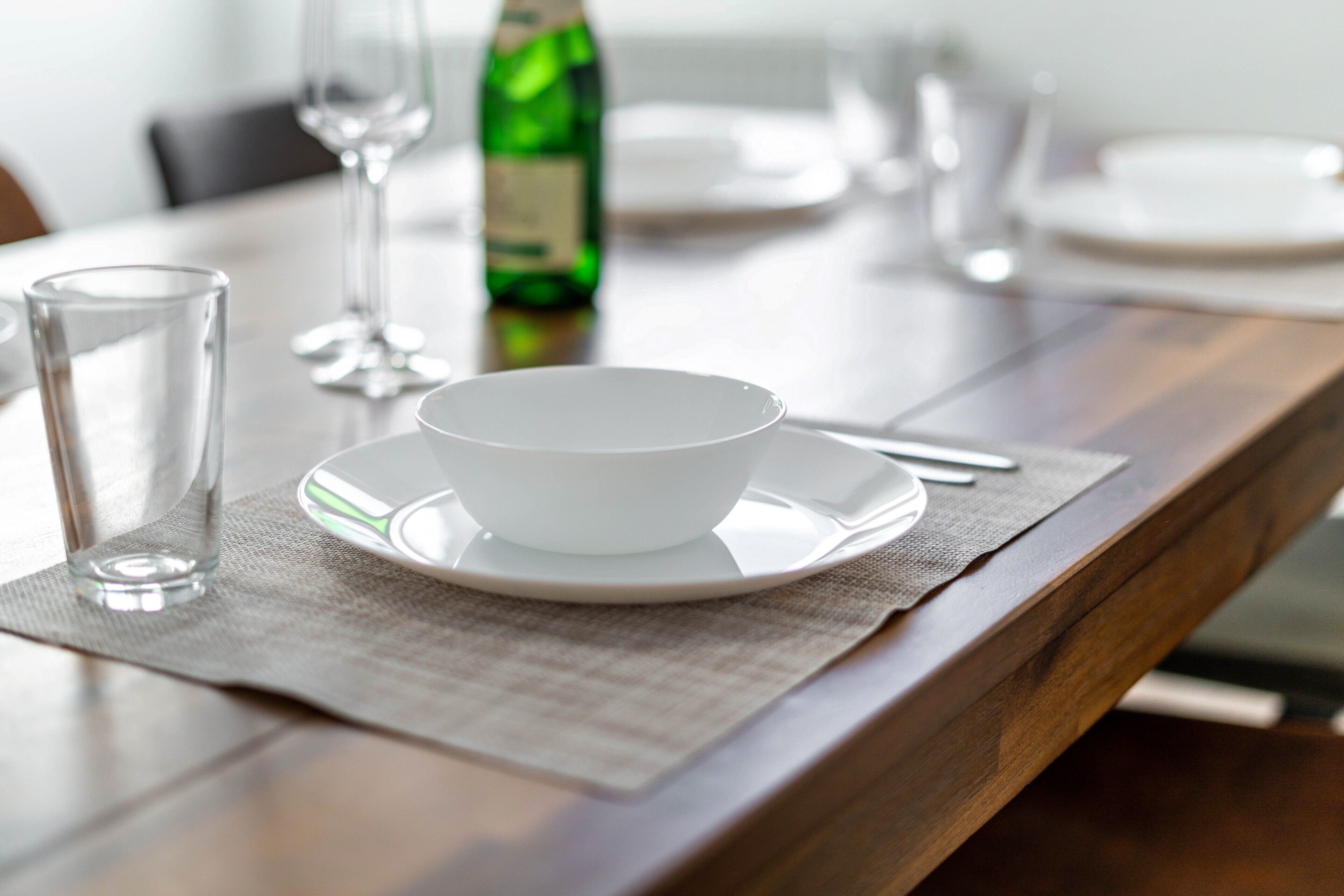 A dining table with a bowl, a glass, and a bottle on a placemat.