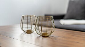 Dos jarrones esquemáticos sobre una mesa de madera en una habitación con un sofá gris y una manta blanca.