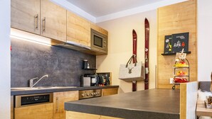 Una cocina con armarios de madera, microondas, cafetera y esquíes colgados en la pared.