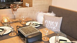 Un comedor con una mesa dispuesta para dos personas, una cabeza de venado decorativa, una vela y un cojín con el texto 'enjoy the little things'.