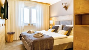 Una habitación de hotel con cama, televisión, ventana con cortinas, cabecero de madera y decoración de cabeza de ciervo montada en la pared.