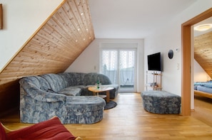 Een kamer in loft-stijl met een schuine plafond, een hoekbank, een klein rond tafeltje, een televisie en een bed.