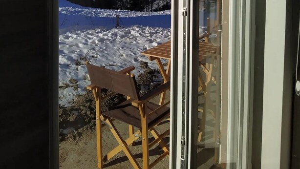 Une pièce dotée d’une porte-fenêtre coulissante qui donne sur un espace extérieur enneigé, où se trouvent un banc et une table.